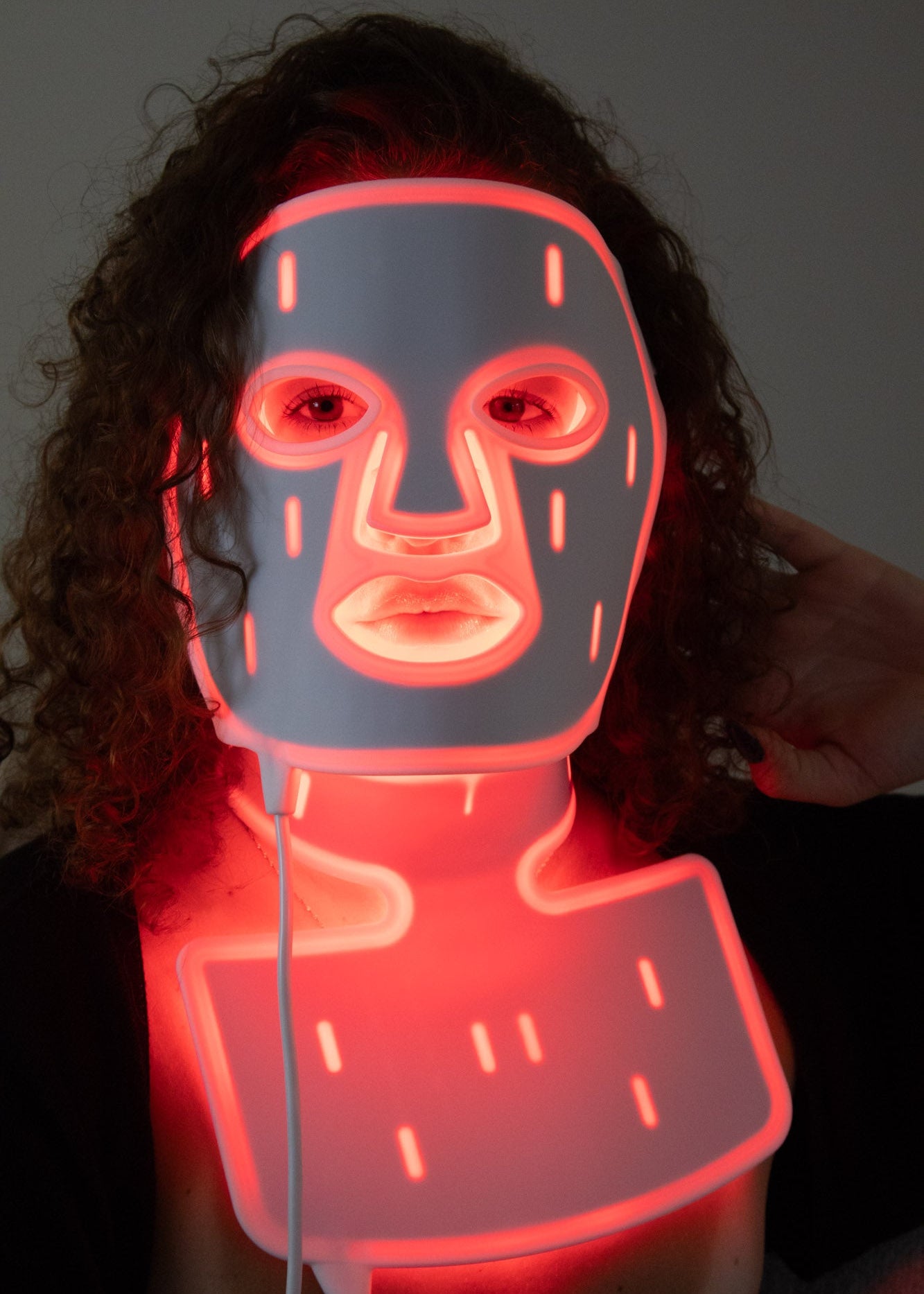 Woman wearing PHOS Complete System face mask and neck treatment with red LED light therapy during evening skincare routine