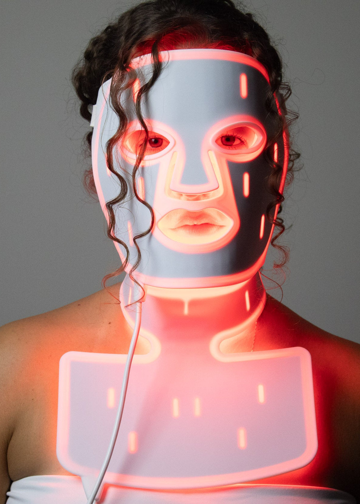 Woman wearing the PHOS Complete System with face mask and neck treatment delivering red LED light therapy across face and décolletage simultaneously