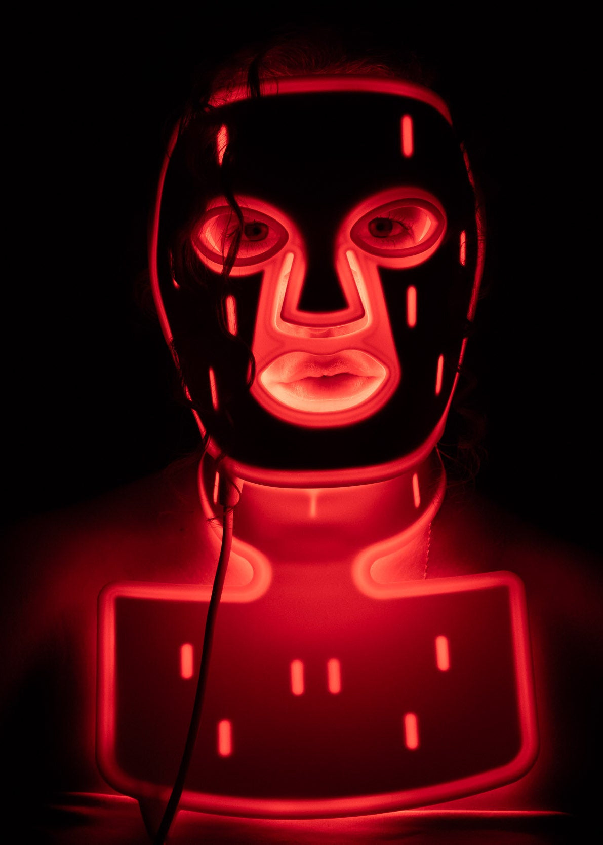 PHOS Complete System face mask and neck treatment glowing red in dark room showing full face-to-décolletage LED coverage