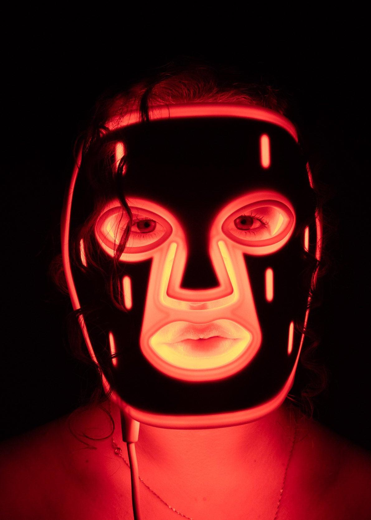 PHOS Face Mask with red LED light therapy glowing in dark room showing full-face coverage