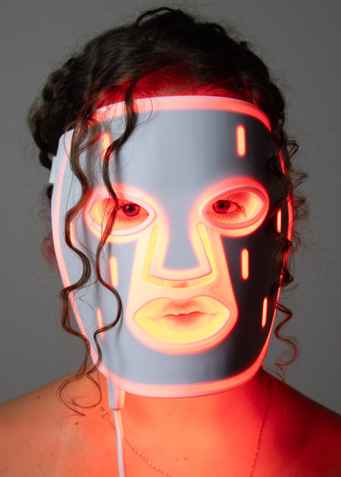 Woman wearing the PHOS Face Mask with red LED light therapy illuminating face — front portrait view