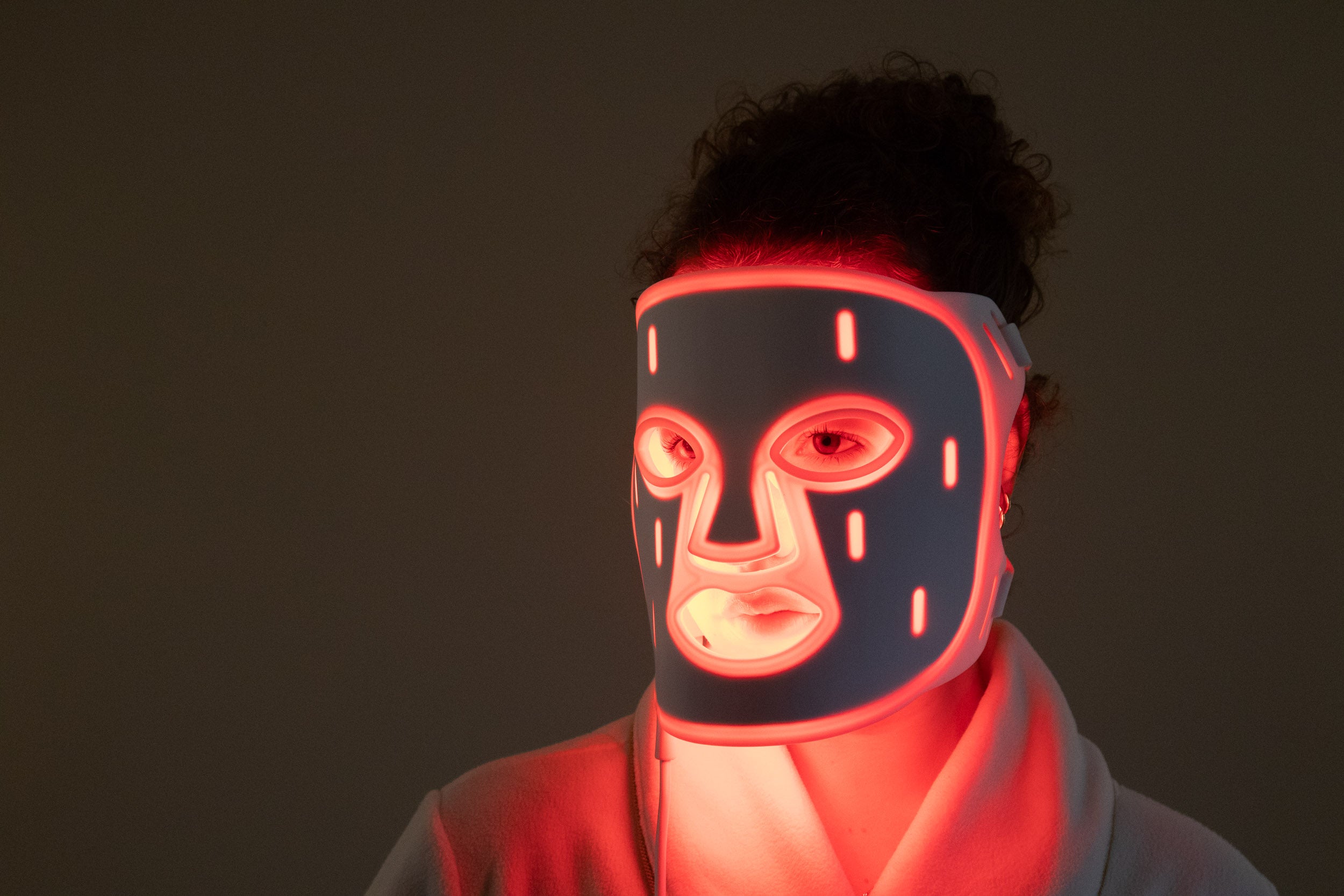 A woman wearing the PHOS LED face mask with red light therapy glowing in a dark room